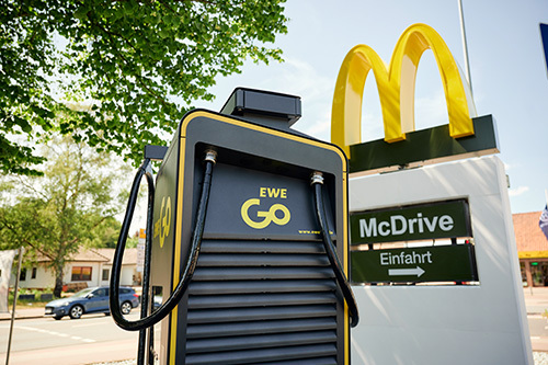 Neben eine Schnellladestation von EWE Go ist ein Logo von McDonald's zu sehen. Die Ladestation befindet sich auf dem Parkplatz eines McDrive-Restaurants.