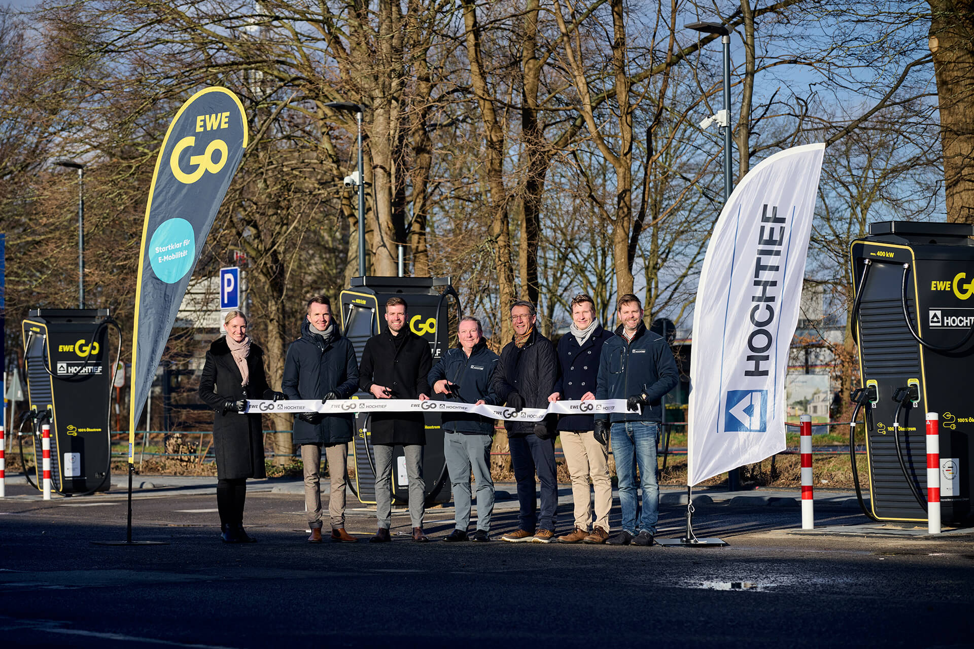 Feierliche Eröffnung eines Ladeparks des Deutschlandnetzes in Lübbecke: Vertreter von EWE Go und HOCHTIEF stehen vor modernen Schnellladestationen für E-Autos. Der Ladepark bietet vier Hypercharger mit mindestens 200 kW Ladeleistung und 100 % Ökostrom für schnelles und nachhaltiges Laden.